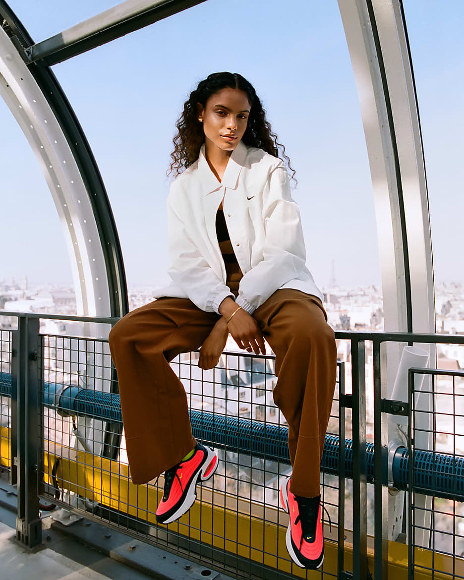 Woman in a white jacket and brown pants wearing bright sneakers, showcasing trendy streetwear style.